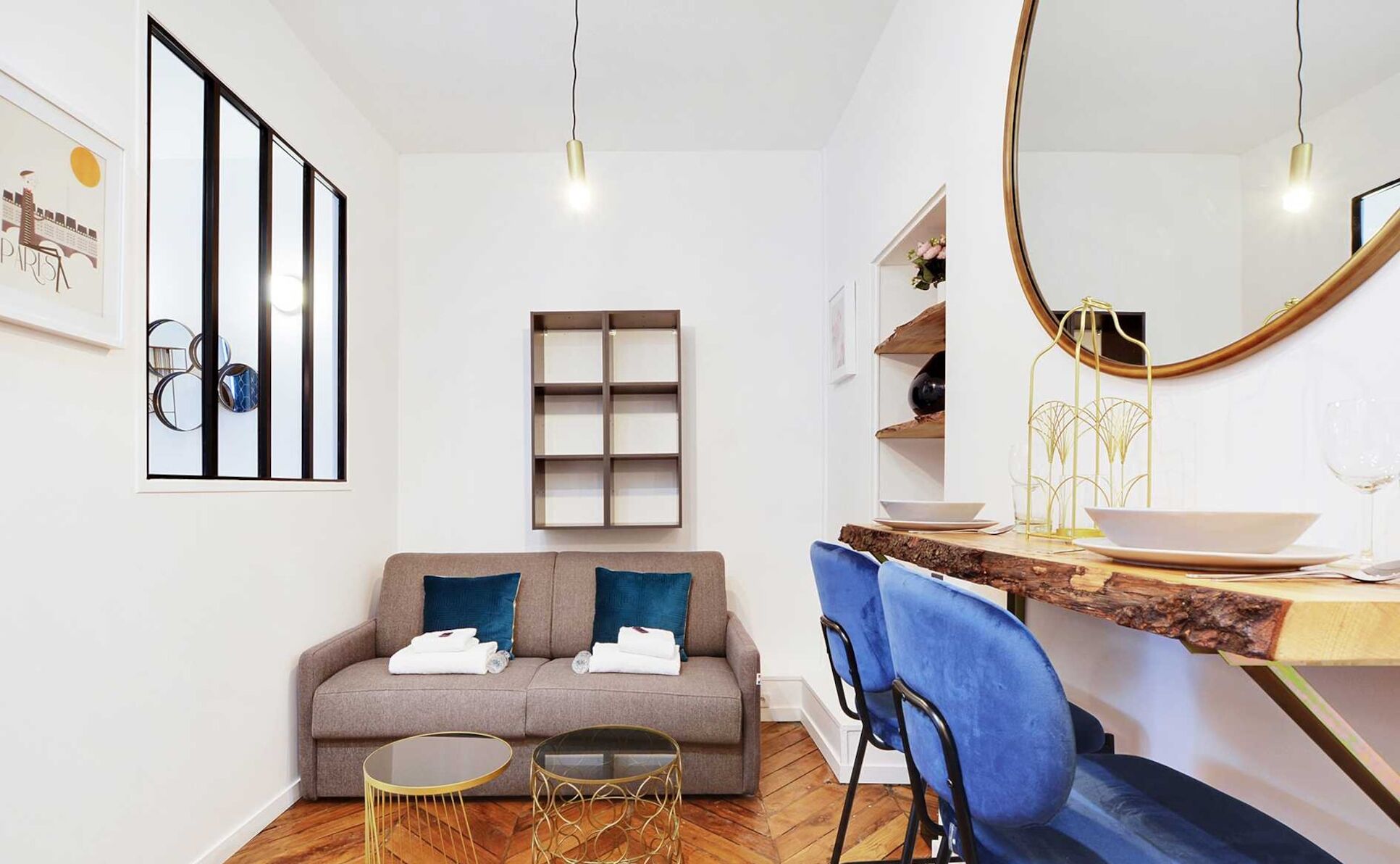 Een moderne woonkamer met een bank, twee kleine tafels, een blauwe fauteuil, een houten eettafel en een grote spiegel.