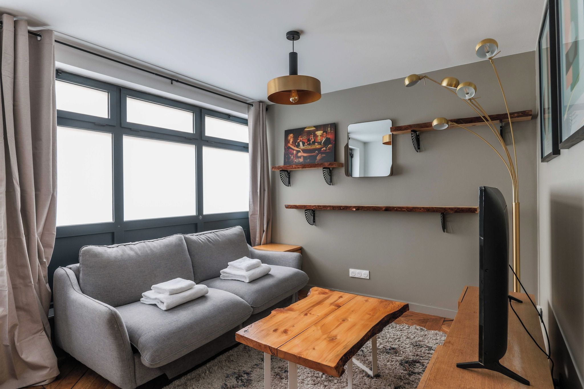 Un salon moderne avec un canapé gris, une table basse en bois, un téléviseur à écran plat et un luminaire suspendu.
