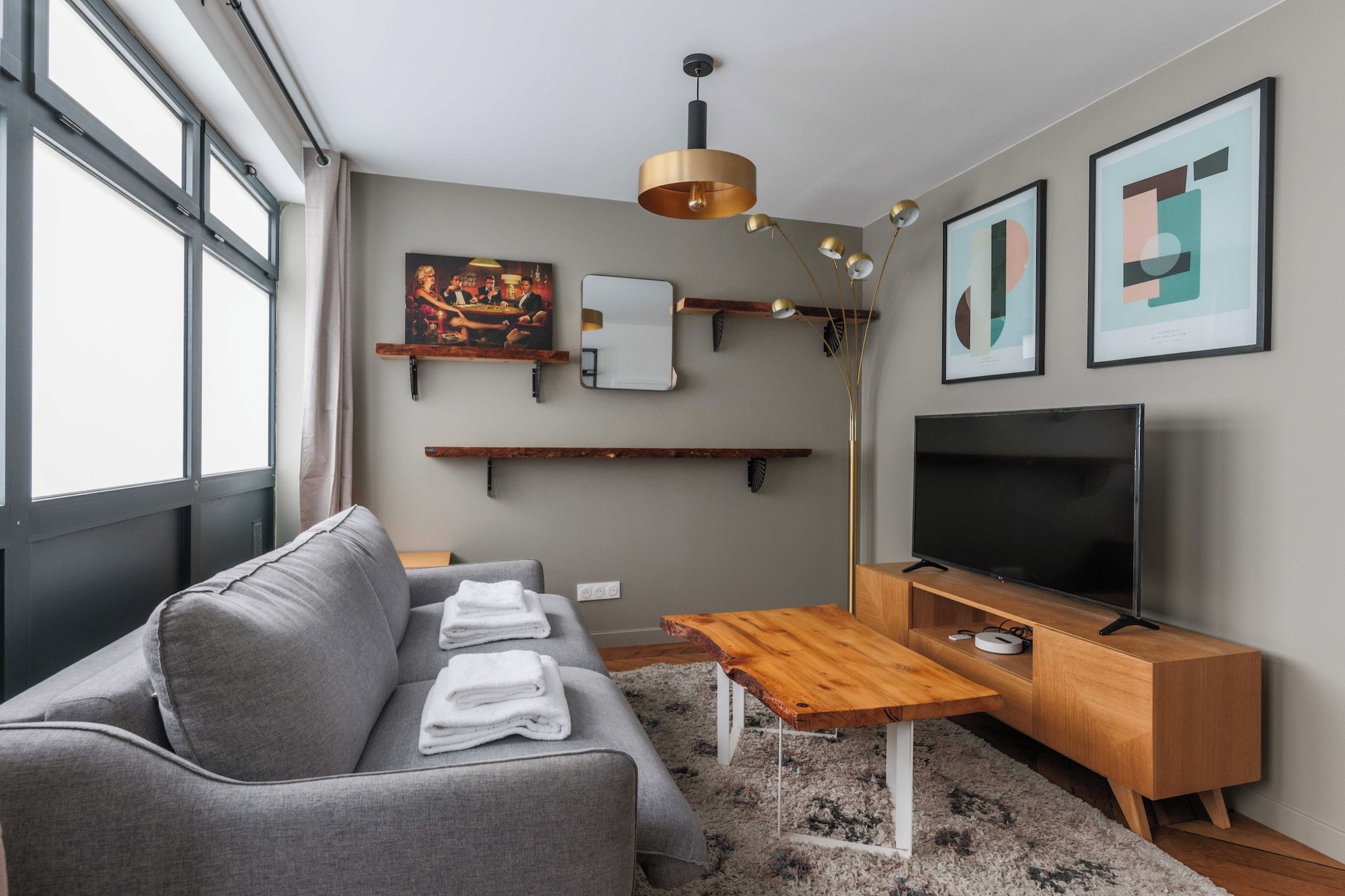 A modern living room with a grey sofa, a wooden coffee table, a flat-screen TV, and artwork on the walls.