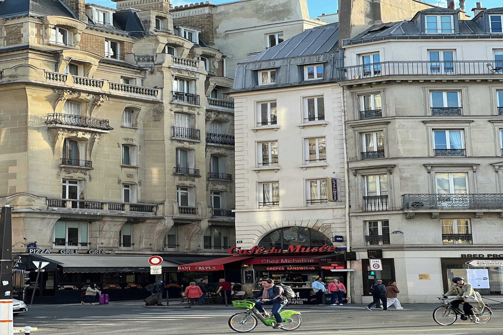 Une vue de rue avec un café appelé « Café du Musée » et un restaurant de pizzas.