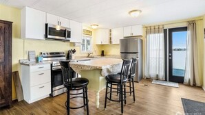 A compact kitchen with white cabinets, a microwave, a stove, a refrigerator, and a small island with bar stools. - Sunset Paradise (Moses Lake)