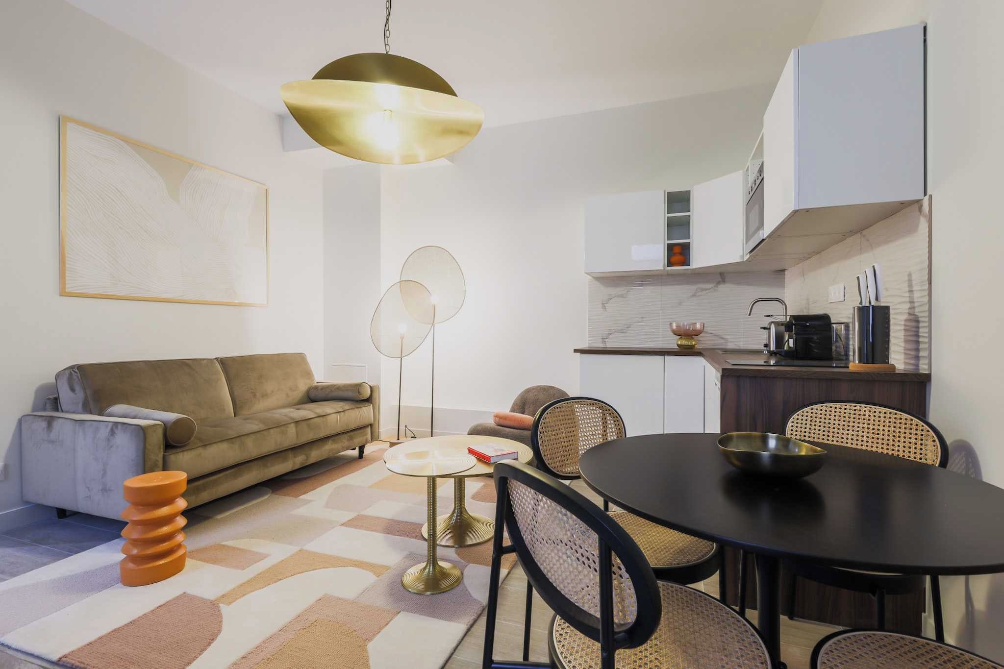Un espace de vie compact comprenant un canapé, une table à manger, des chaises, une machine à café et un coin cuisine.