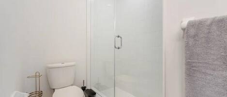 Une salle de bain équipée de toilettes, d’une douche à parois de verre et d’un porte-serviettes.