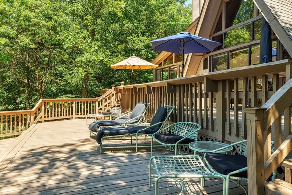A wooden deck with outdoor seating, including lounge chairs and a table, surrounded by a wooden fence and trees.