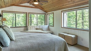 A bedroom with a large bed, a ceiling fan, and multiple windows offering a view of the outdoors. - Foxtail Lake Front Chalet with HOT TUB (Innsbrook)