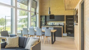 Une cuisine moderne dotée d’un îlot central, de grandes fenêtres et d’un coin repas avec un canapé et des fauteuils.