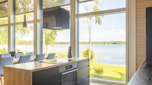 Une cuisine moderne dotée de grandes fenêtres donnant sur un lac, un coin repas avec des chaises et un four encastré.