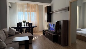 A modern living room with a sofa, a dining table with chairs, a flat-screen TV, and a wooden cabinet.