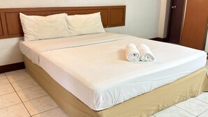 A neatly made bed with a wooden headboard, white bedding, and two rolled towels on the bed.