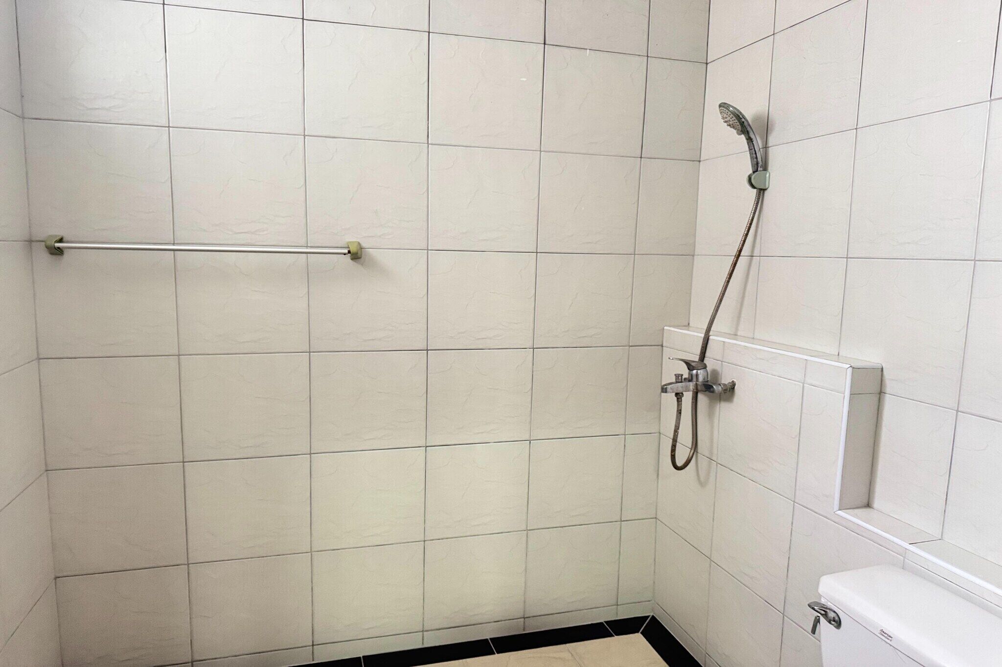 Een badkamer met witte betegelde wanden, een douche met een handdouche en een toilet.