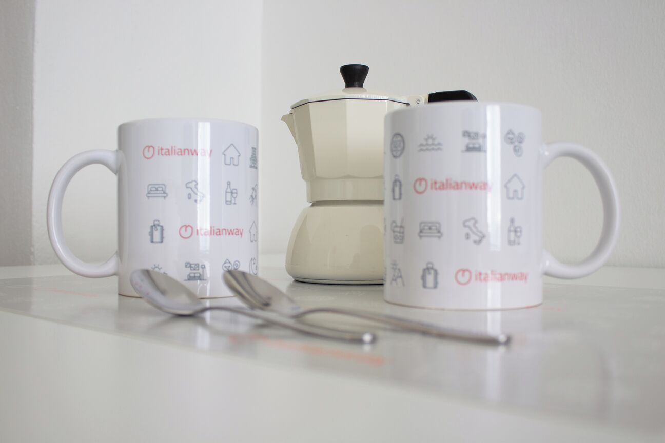 Two white mugs with Italian symbols and text, a white teapot, and a spoon on a table.
