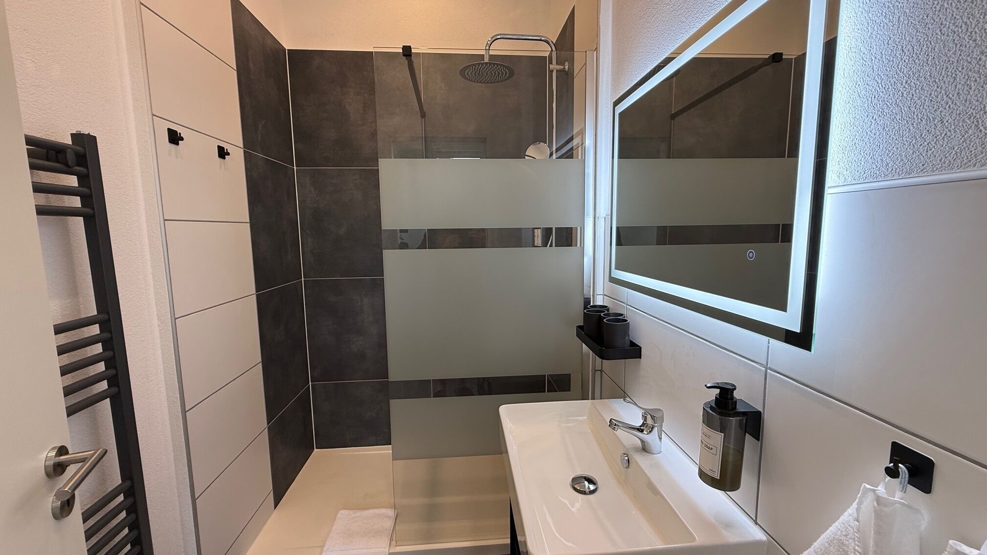Een moderne badkamer met een glazen douchecabine, een wit wastafelmeubel met spiegel en een handdoekrek.