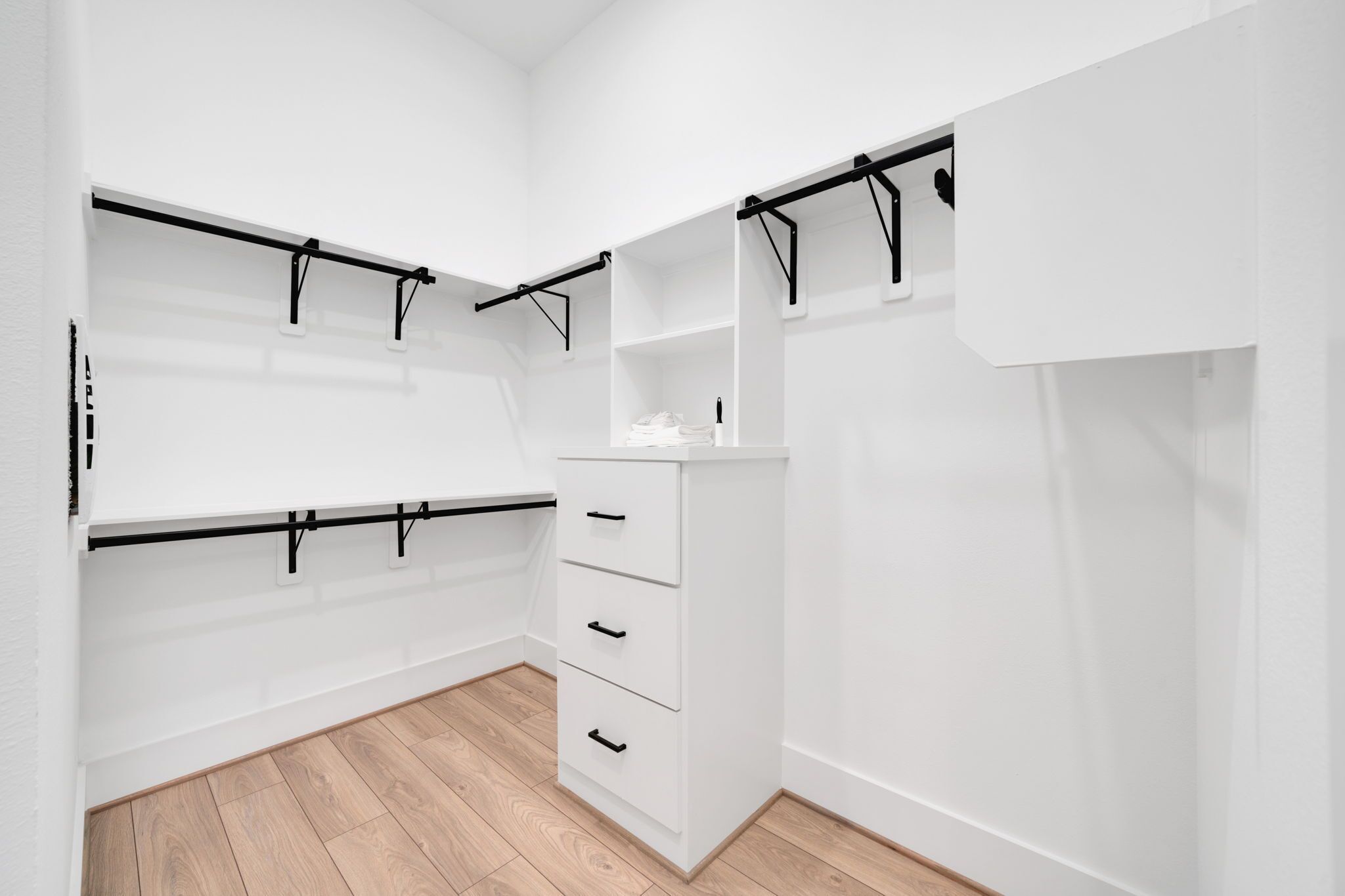 A white walk-in closet with multiple shelves, drawers, and a hanging rod.