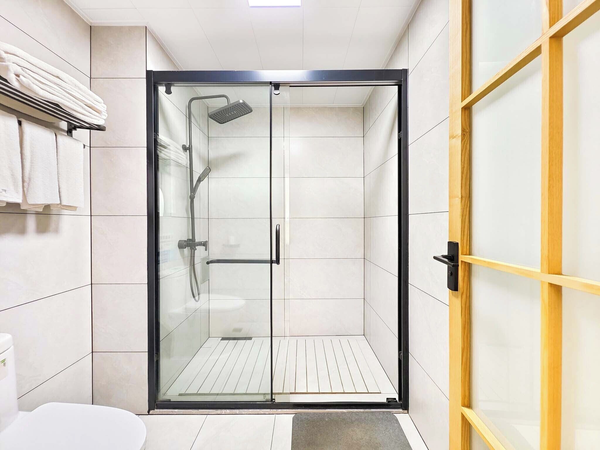 Une salle de bain moderne avec une douche à parois de verre, des carreaux blancs et un cadre de porte en bois.