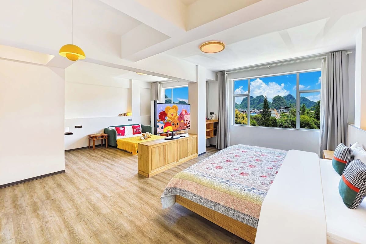 A modern hotel room with a large bed, a desk, a TV, and a view of the mountains.