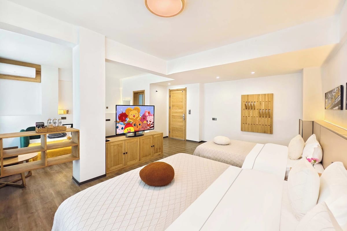 A modern hotel room with a large bed, a TV, a wooden desk, and a wall-mounted light fixture.