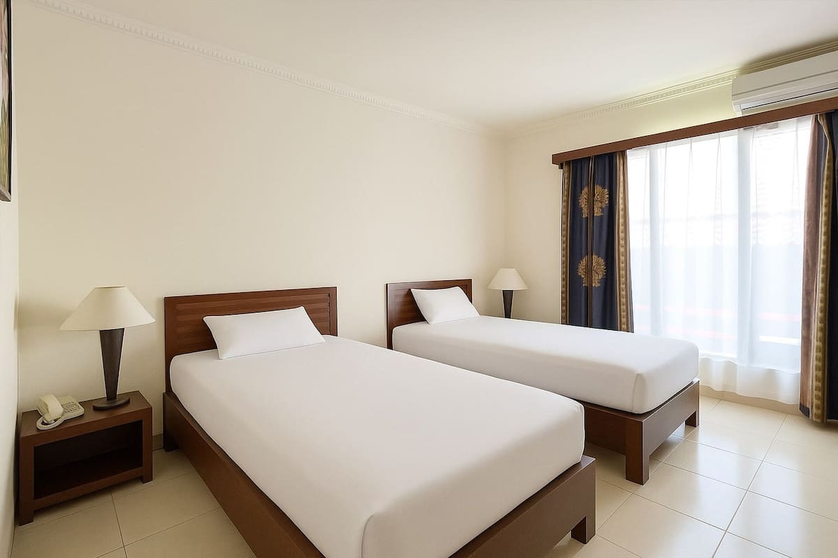 A hotel room with two single beds, a nightstand with a lamp, a telephone, and a window with curtains.