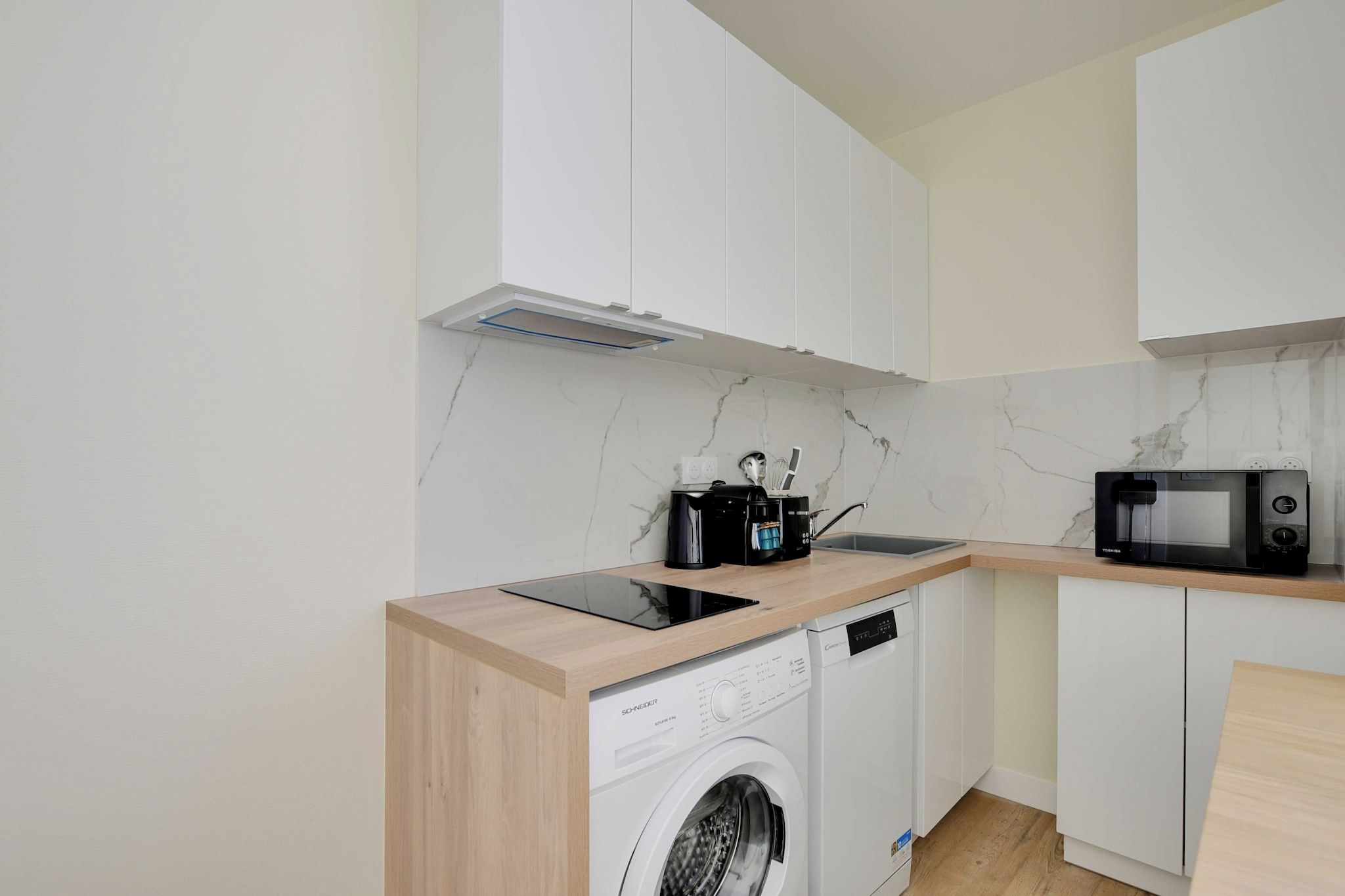 Une cuisine compacte équipée d’un lave-linge, d’un four à micro-ondes et d’une machine à café posée sur le plan de travail.