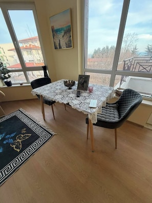 A dining area with a table covered by a lace tablecloth, two chairs, a bowl, a picture frame, and a remote control.
