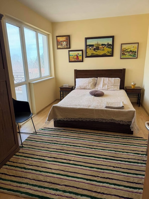 A bedroom with a large bed, a window, and three framed paintings on the wall.