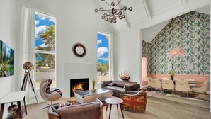 Un salon spacieux doté d’une cheminée, de canapés en cuir, d’un coin repas et d’une grande fenêtre offrant une vue sur les arbres.