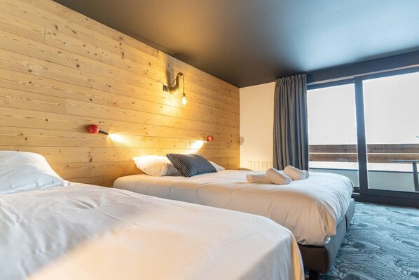 A hotel room with two beds, wooden panel walls, a large window with curtains, and a balcony. - Delightful apartment in Saint Chaffrey (SAINT CHAFFREY)