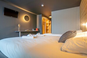A hotel room with a bed, a TV, a mirror, a towel rack, a shelf with toiletries, and a patterned headboard. - Delightful apartment in Saint Chaffrey (SAINT CHAFFREY)