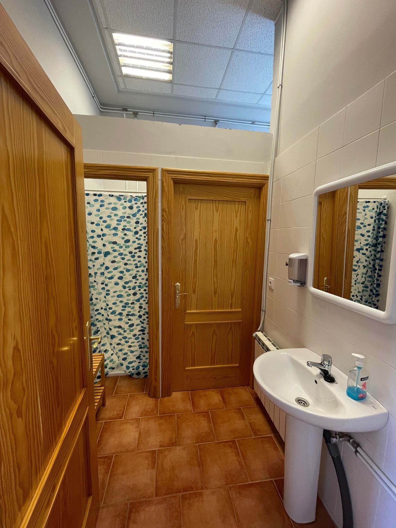 A bathroom with a wooden door, a white sink, and a mirror above it.