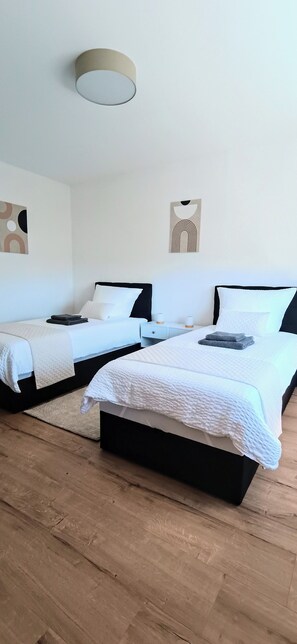 A hotel room with two beds, a wooden floor, and a ceiling light fixture.