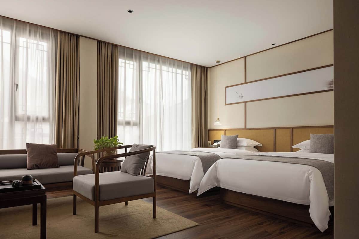 A hotel room with two beds, a sofa, a chair, a small table, and a potted plant.