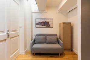 A room with a grey sofa, a wooden cabinet, and a framed picture of beach huts on the wall.