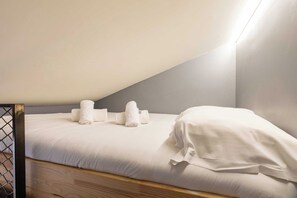 A neatly made bed with white bedding and two rolled towels placed on it.