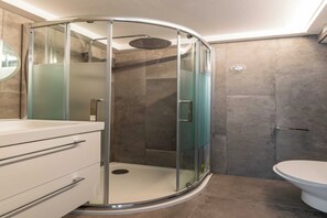 A modern bathroom with a glass-enclosed shower, a toilet, and a vanity with drawers.