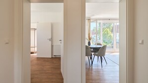 A modern interior with a wooden floor, a dining area with a table and chairs, and a view of the outdoors through large windows.
