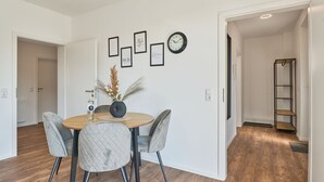 A dining area with a round table, four chairs, a vase with flowers, and framed pictures on the wall.