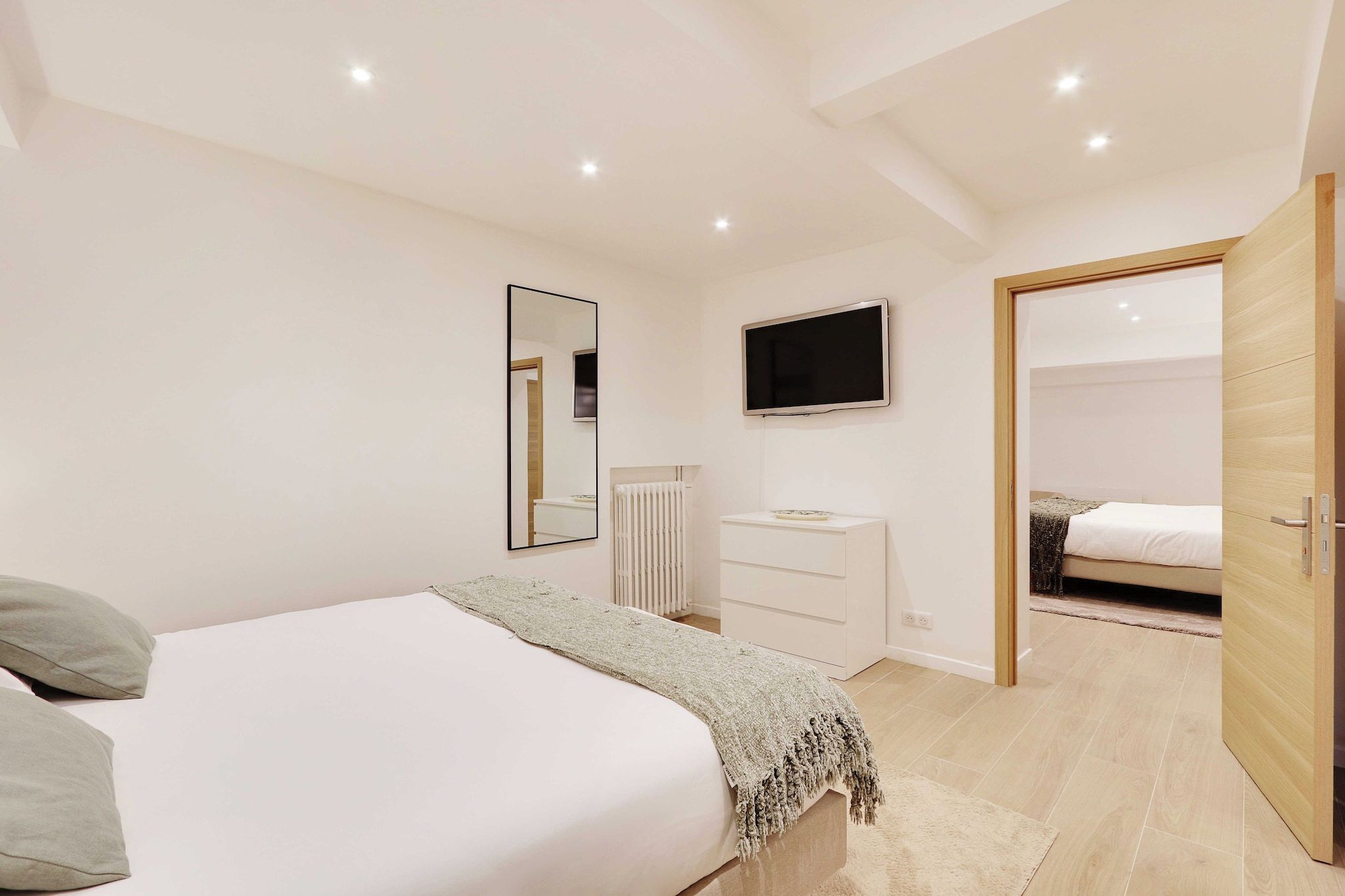 Une chambre à coucher comprenant un lit, une commode, un téléviseur et une porte donnant sur une autre pièce.