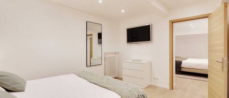 Une chambre à coucher comprenant un lit, une commode, un téléviseur et une porte donnant sur une autre pièce.