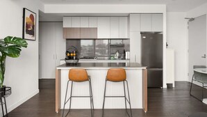 A modern kitchen with a central island, two bar stools, and a stainless steel refrigerator. - Stylish apartment near South Melbourne Market (South Melbourne)