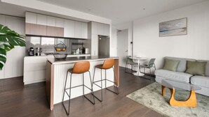 A modern kitchen with a central island, bar stools, and a dining area with a sofa and chairs. - Stylish apartment near South Melbourne Market (South Melbourne)