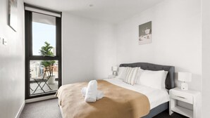 A hotel room with a bed, two bedside tables, a window, and a view of the outside. - Stylish apartment near South Melbourne Market (South Melbourne)