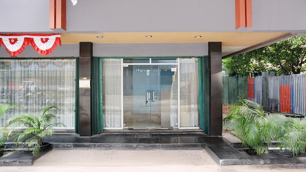 Entrada de hotel con puerta de vidrio, zona de acceso techada y plantas en macetas.