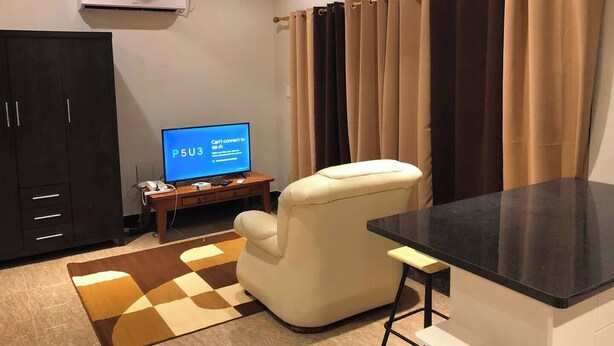 Un salon avec un téléviseur à écran plat affichant un message d’erreur concernant la connexion Wi-Fi, un fauteuil beige, une petite table d’appoint en bois et un tapis à carreaux.