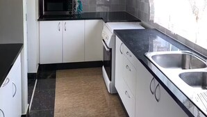 Une cuisine moderne avec des meubles blancs, un plan de travail noir, un évier en acier inoxydable et un four à micro-ondes.