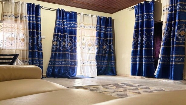 A room with a beige sofa, patterned curtains, and a tiled floor. - Serene Room and Living Room (Serrekunda)