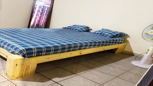 A single bed with a plaid bedspread and matching pillows, a wooden frame, and a tiled floor. - Serene Room and Living Room (Serrekunda)