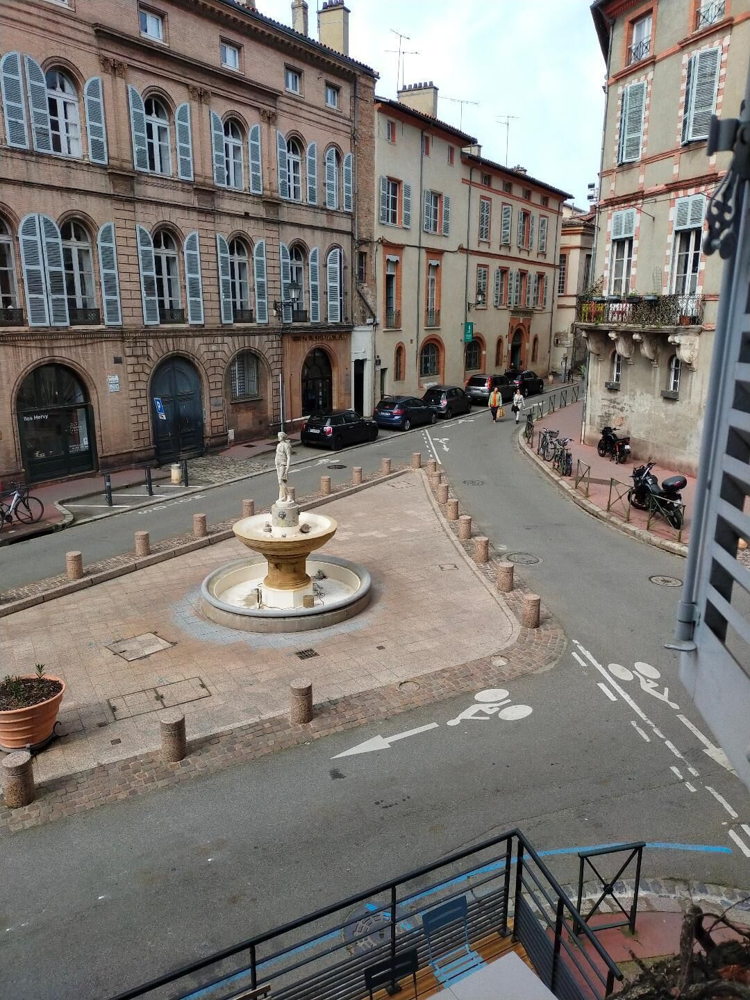 A public square with a central fountain, surrounded by historic buildings with arched windows and balconies.