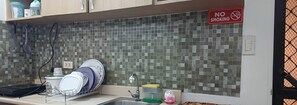 Una cucina con pareti rivestite di piastrelle, un espositore per piatti, un lavandino e un piano di lavoro con diversi oggetti.