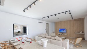Una sala de estar moderna con un sofá, una mesa de comedor dispuesta con platos y vasos, y un televisor montado en la pared.