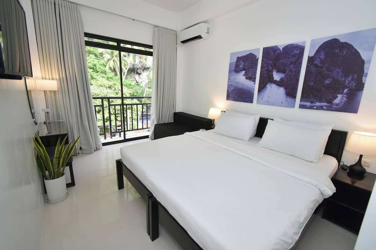 A modern hotel room with a large bed, a balcony with curtains, a potted plant, and a wall with three photographs.