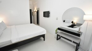 A modern bedroom with a bed, a bedside table, a mirror, and a wall-mounted TV. - BonBob Inn (El Nido)